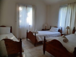 Ett hotellrum med tre sängar i trä, vita sängkläder och gardiner.