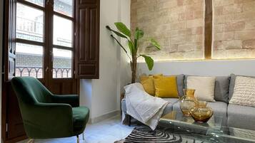 Una sala de estar con un sillón verde, un sofá con cojines, una mesa de centro de vidrio y una alfombra con estampado de cebra.