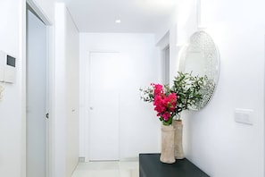 A hallway with a white door, a black console table with a vase of pink flowers, and a decorative mirror on the wall. - Riad Alhambra 3 (granada)