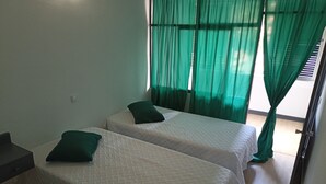 Una habitación con dos camas individuales, cada una con almohada verde, ropa de cama blanca y cortinas verdes traslúcidas.