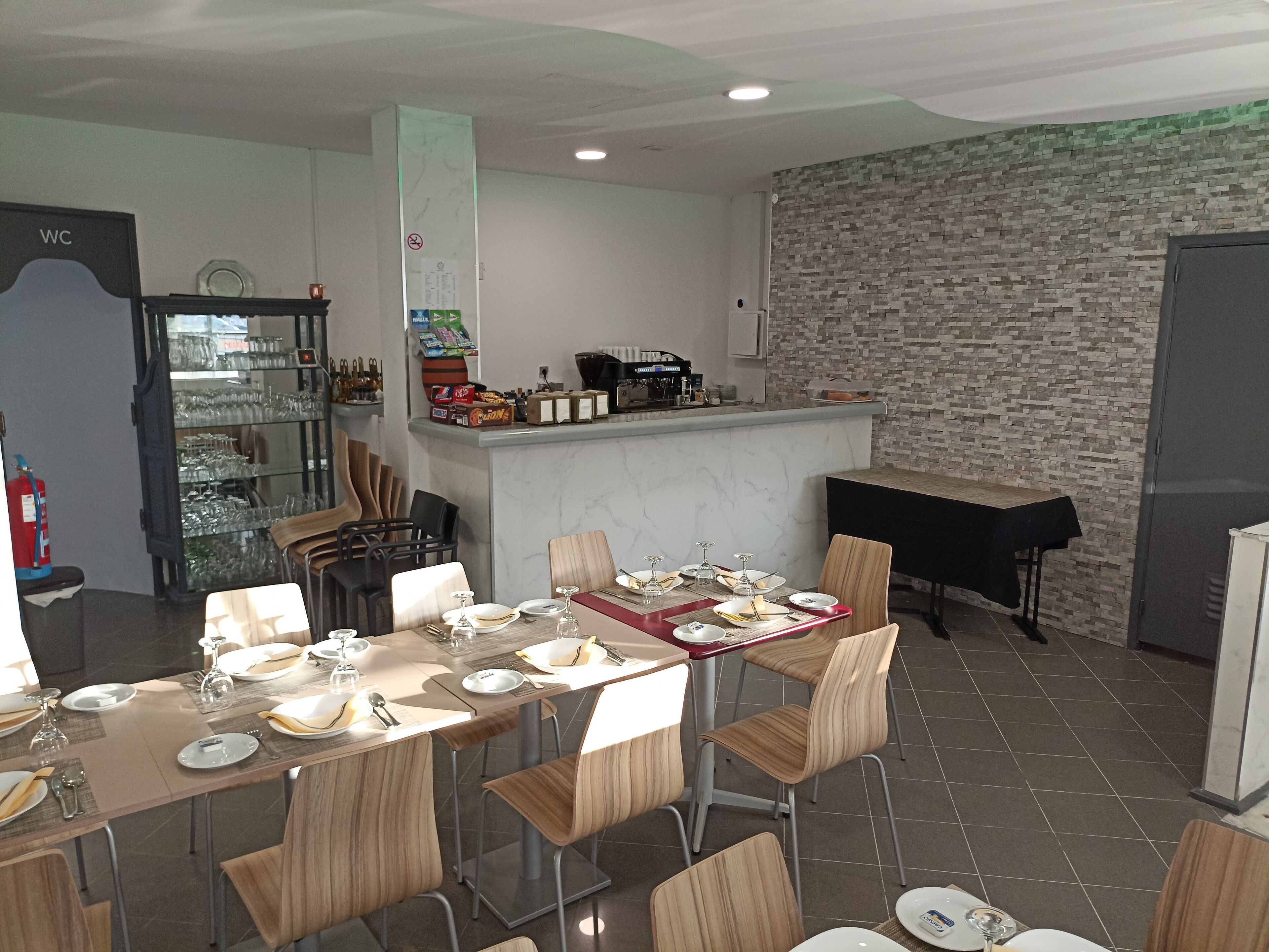 Un comedor con una mesa larga dispuesta para una comida, sillas, una barra con una máquina de café y una pared con diseño de ladrillo.