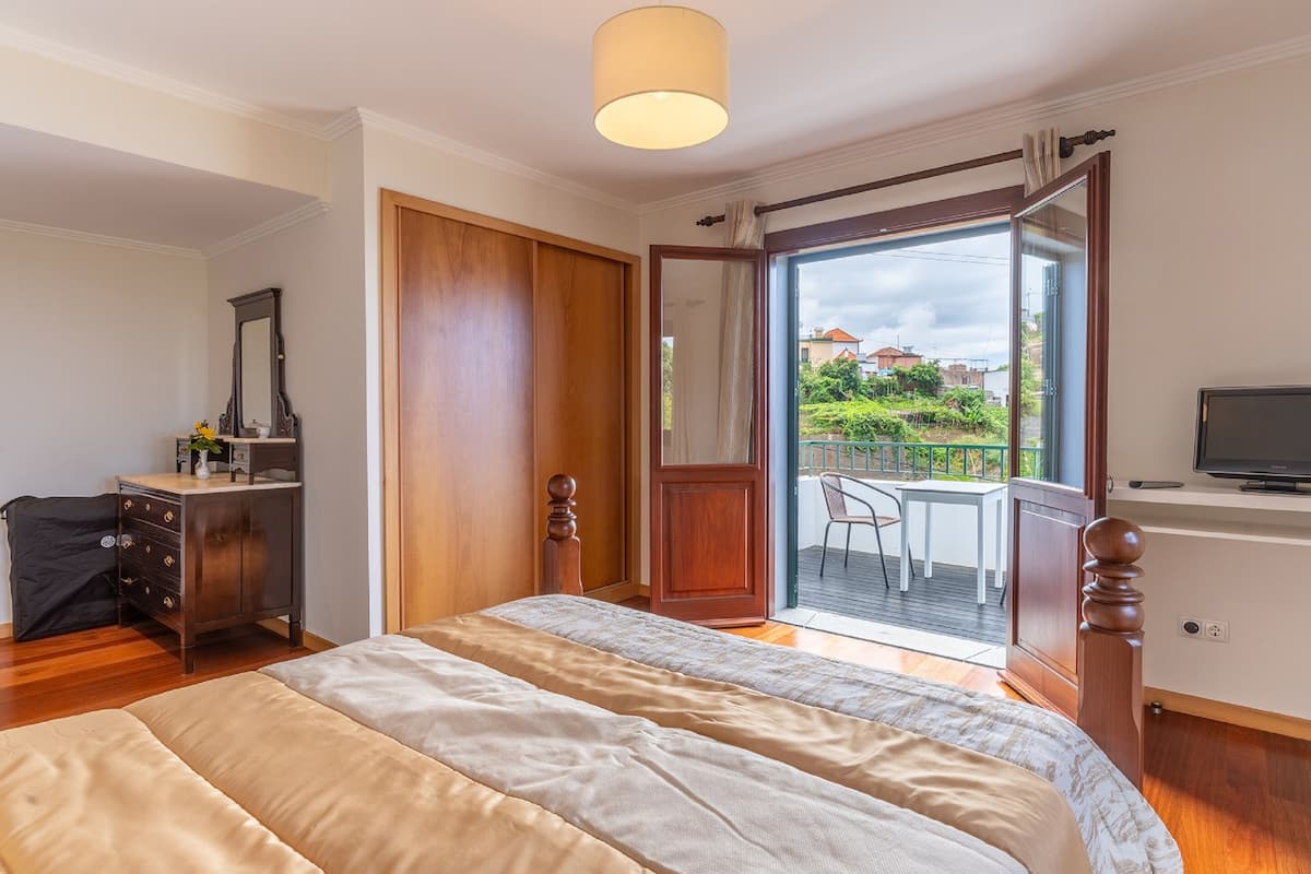 Ein Schlafzimmer mit Bett, Schreibtisch, Fernseher und einem Balkon mit Außenblick.