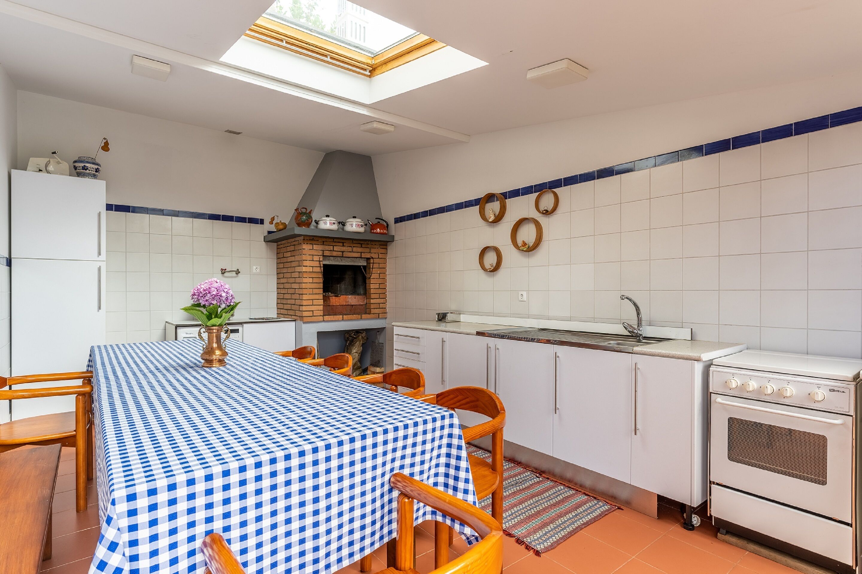 A kitchen with a checkered tablecloth, a brick oven, white cabinets, and a skylight.