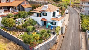 A two-story house with a tiled roof, a balcony, and a small garden area. - Villa Dinis (Calheta)