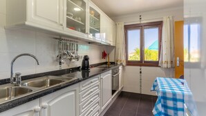 A kitchen with white cabinets, stainless steel sinks, and a window with curtains. - Villa Dinis (Calheta)