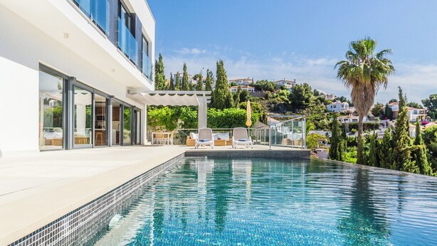 A modern building with a swimming pool, outdoor seating, and a view of a hillside with houses. - Villa La Perla with private heated pool and great views (Salobreña)