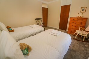 A bedroom with two single beds, a wooden dresser, a rocking chair, and a teddy bear on one bed.