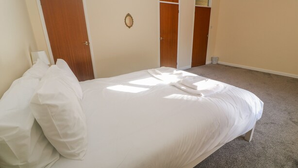 Ein ordentlich bezogenes Bett in einem Hotelzimmer mit Teppichboden, Holztüren und einer kleinen Mülltonne.