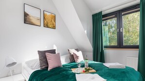 A bedroom with a bed, pillows, a bedside table, a lamp, a window with curtains, and two framed pictures on the wall.