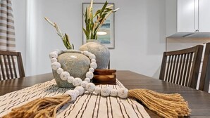 A dining table with a woven placemat, two stone vases with plants, and a wooden coaster.