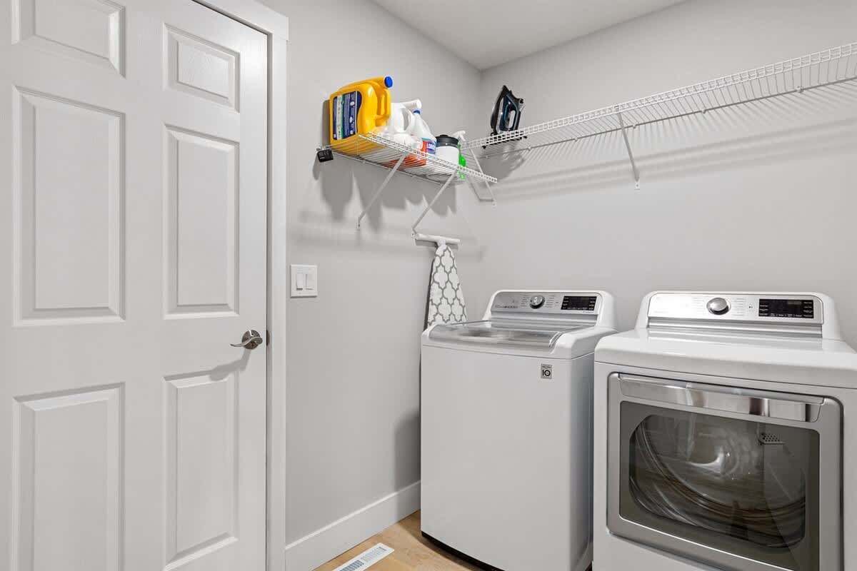A laundry area with two washing machines, a drying rack, and a shelf with cleaning supplies.