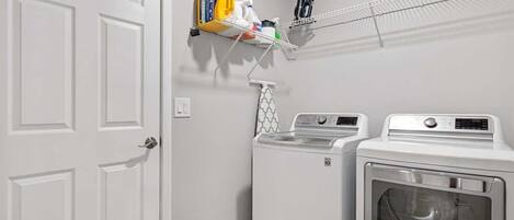 A laundry area with two washing machines, a drying rack, and a shelf with cleaning supplies.