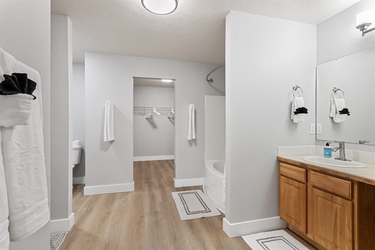 Une salle de bain moderne avec un plancher en bois, des murs blancs, un grand miroir, un lavabo et un espace douche.