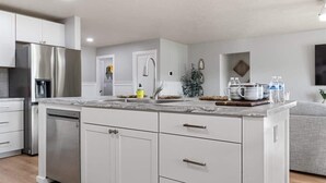 A modern kitchen with white cabinetry, stainless appliances, and a marble countertop.