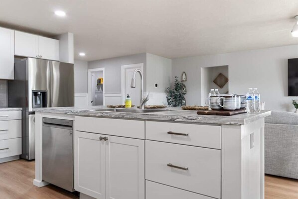 A modern kitchen with white cabinetry, stainless appliances, and a marble countertop.