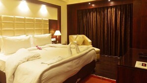Une chambre d’hôtel avec un grand lit, une table de chevet avec une lampe, une chaise et un rideau foncé.