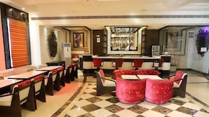 Un hall d’hôtel avec un sol à carreaux, des sièges rouges et noirs, un coin bar et un grand miroir.
