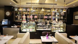 Une boulangerie avec des espaces pour s’asseoir, des présentoirs remplis de produits de boulangerie et des lampes suspendues décoratives.