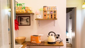 A kitchenette with a bread box, a kettle, and a shelf with tea and coffee products.