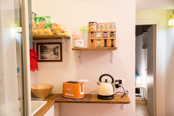 A kitchenette with a bread box, a kettle, and a shelf with tea and coffee products. - Guest Art - Naples (Napoli)