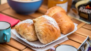 A tray with croissants, a jar of honey, and a coffee mug on a wooden table.
