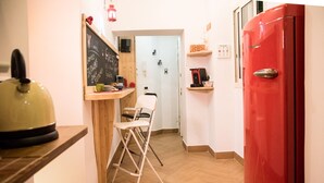 A compact kitchen with a red refrigerator, a small dining area with a chair, and a chalkboard with writing.
