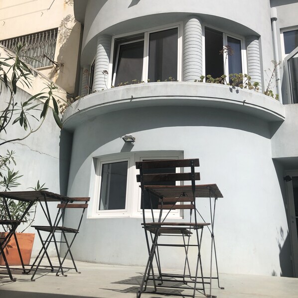 A building with a curved balcony, a small window, and two folding chairs.
