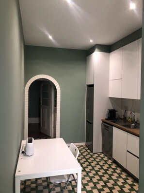 A compact kitchen with a white table, a coffee maker, and a refrigerator.