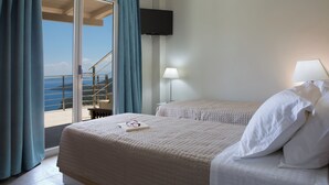 Habitación de hotel con cama, televisión montada en la pared, lámpara y vista al mar desde un balcón.
