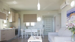 Una cocina moderna con armarios blancos, un comedor con mesa y sillas blancas, y una sala de estar con un sofá gris y un jarrón de flores.