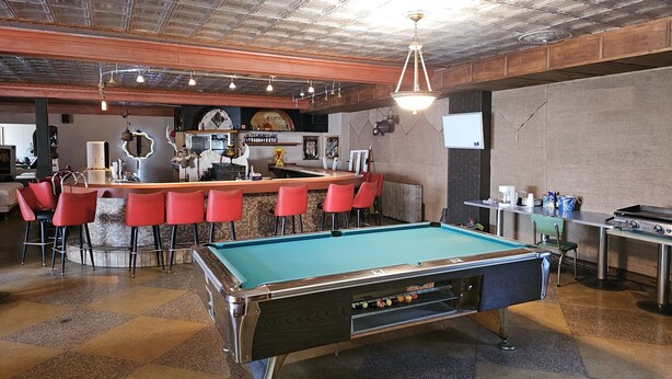 A pool table in a bar area with red chairs and a bar counter.