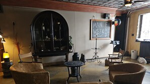 A cozy room with two armchairs, a small round table, and a bookshelf. A chalkboard with 'MAN WEEK' written on it is visible on the wall.