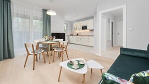 A modern living room with a dining area, a kitchen in the background, and a green sofa.