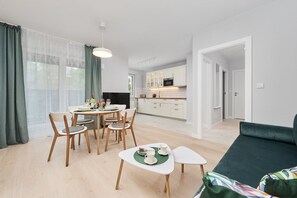 A modern living room with a dining area, a kitchen in the background, and a green sofa.