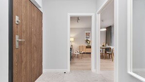 A hallway leading to a dining area with a wooden door, a white wall, and a tiled floor.