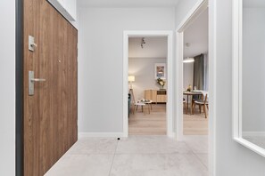Un corridoio che conduce a una sala da pranzo, con una porta in legno, un muro bianco e un pavimento piastrellato.