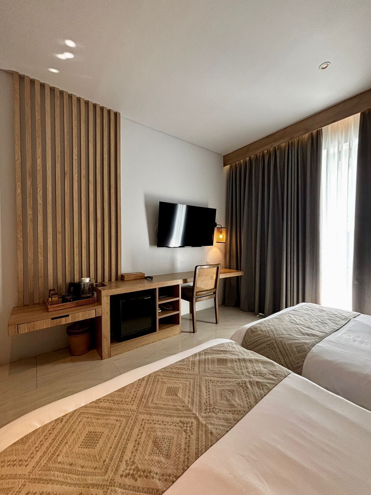 A hotel room with a TV, a desk with a chair, a bed, and a large window with curtains.