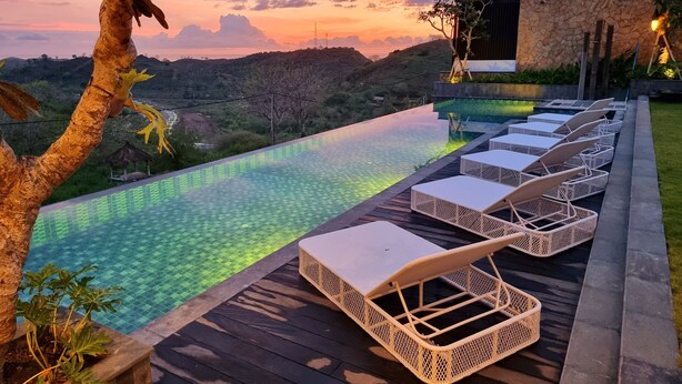 Une piscine à débordement dotée de chaises longues, entourée d’une terrasse en bois et d’un mur de pierre, offrant une vue imprenable sur un paysage magnifique.