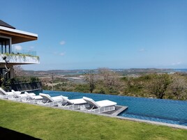 Una piscina infinita con sillas de descanso blancas, vistas despejadas del paisaje y un edificio moderno con balcón.
