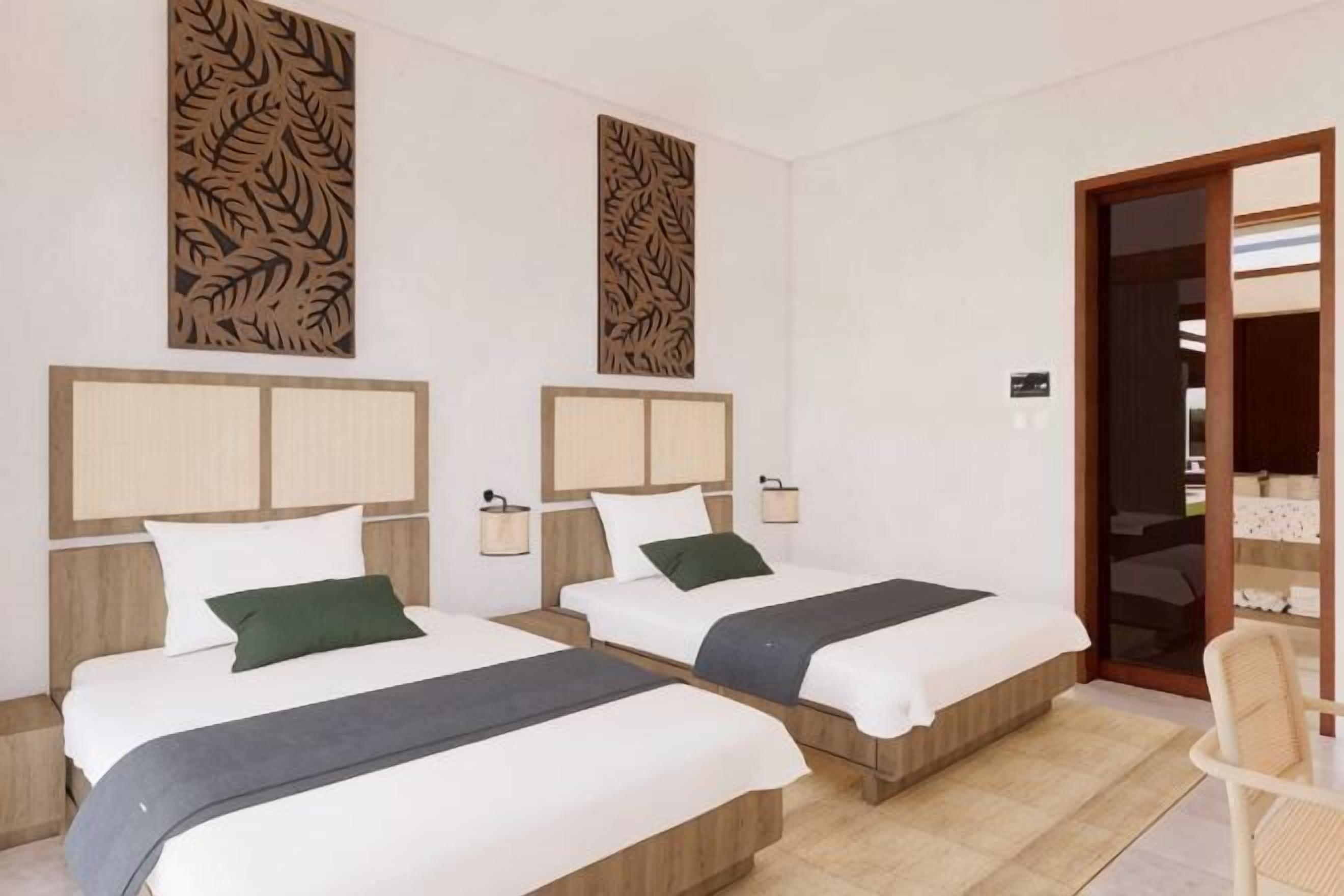 A hotel room with two beds, a wooden headboard, a small table, and a chair.