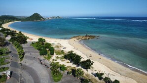 Une plage côtière avec une rive incurvée, une vue dégagée sur l’océan et une route bordée de véhicules garés.