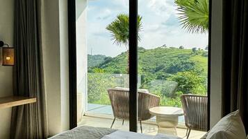 A hotel room with a bed, a small table, and a view of a lush landscape through a large window.
