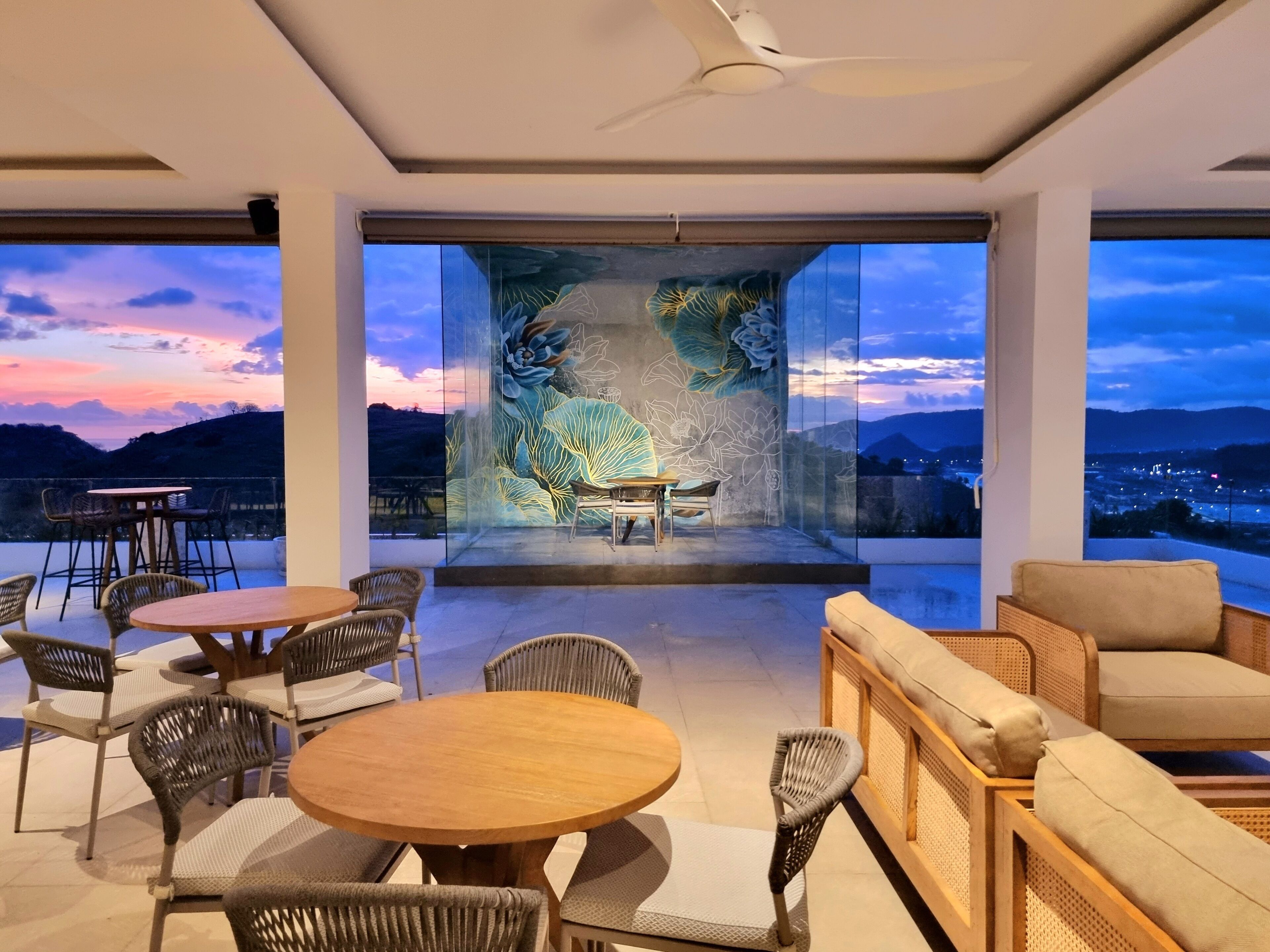 A modern outdoor seating area with wicker furniture and a view of a sunset over hills.