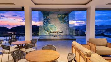 A modern outdoor seating area with wicker furniture and a view of a sunset over hills.