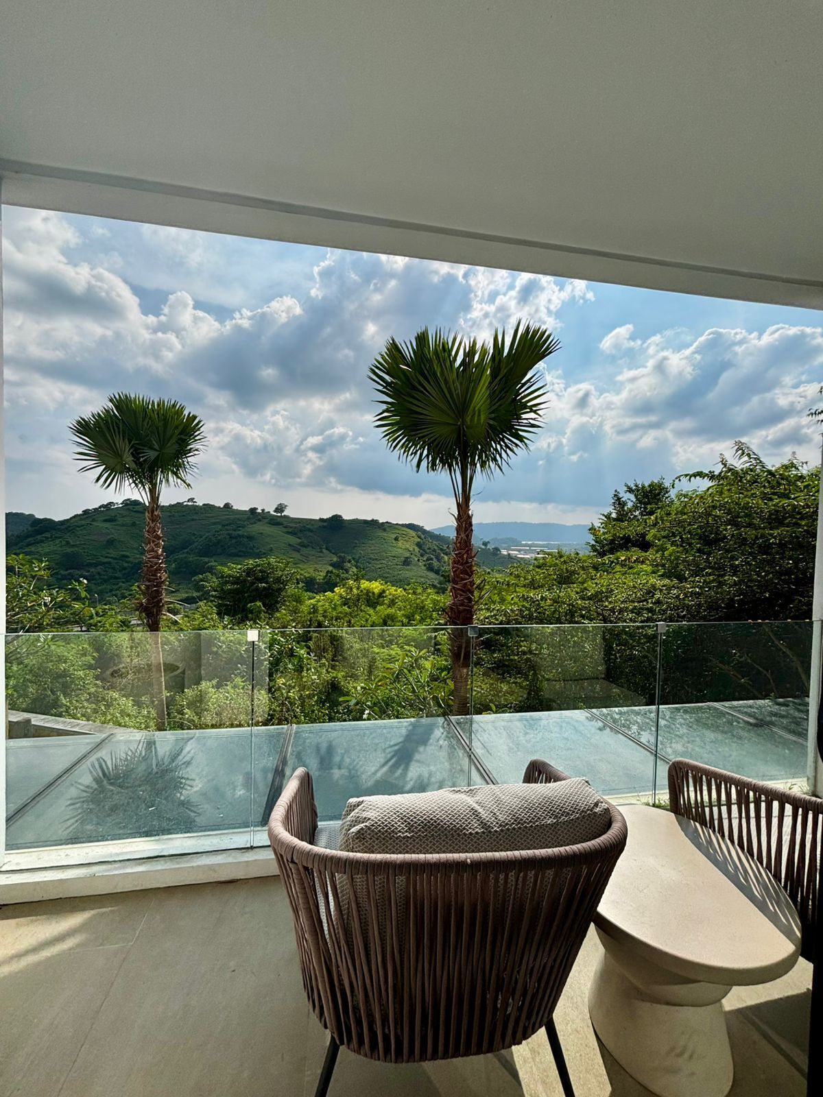 Un balcón con sillas de mimbre y vistas a un paisaje exuberante con palmeras y colinas.