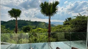 Un balcón con sillas de mimbre y vistas a un paisaje exuberante con palmeras y colinas.