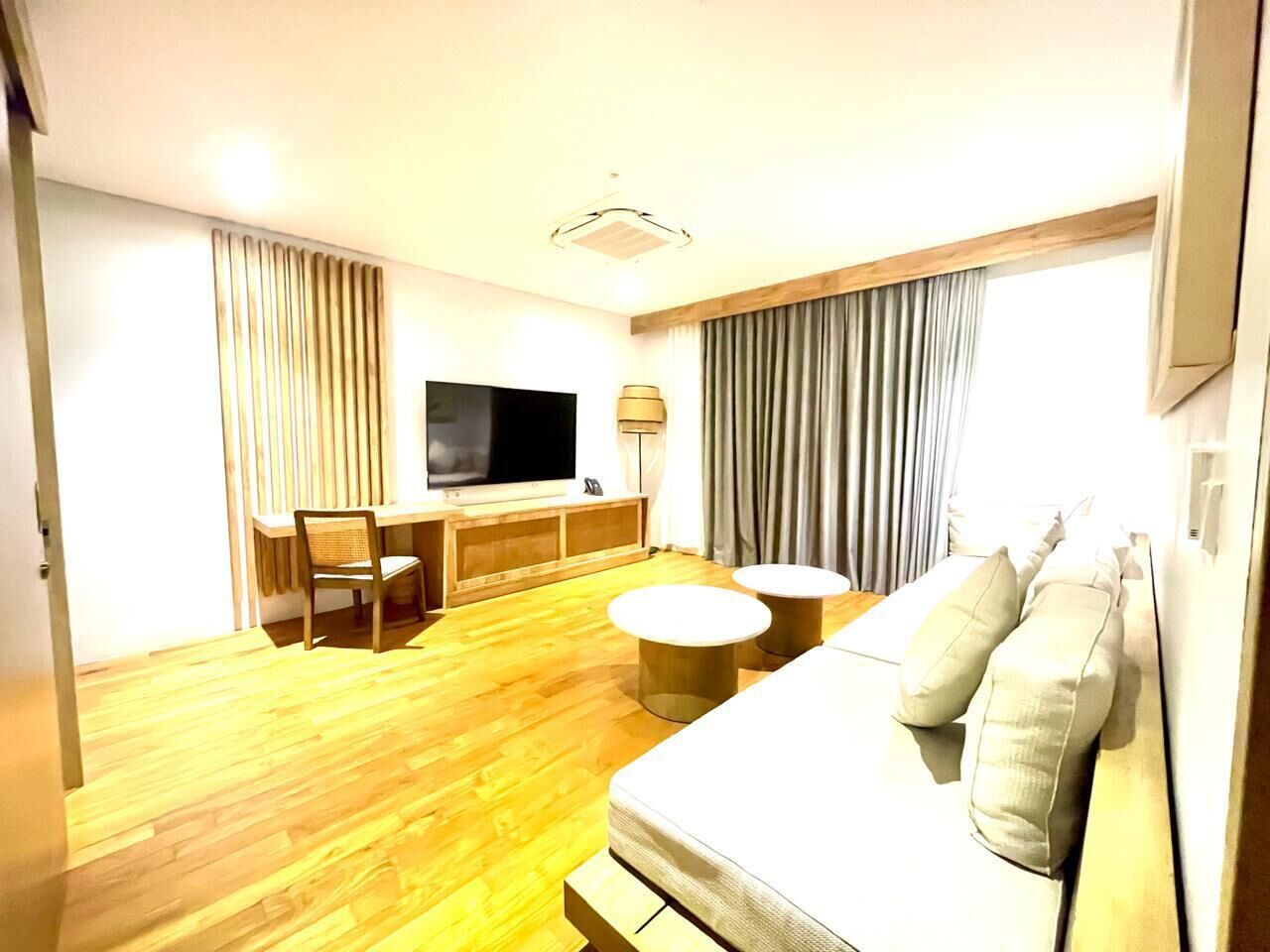 Una habitación de hotel con piso de madera, un sofá, un televisor, un escritorio y una silla.