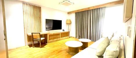Una habitación de hotel con piso de madera, un sofá, un televisor, un escritorio y una silla.