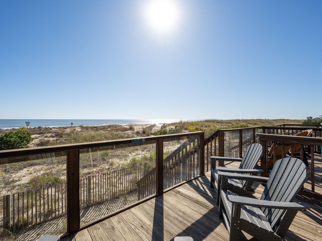 Terraza de madera con sillas Adirondack con vista a la playa.