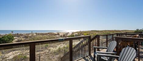 Terraza de madera con sillas Adirondack con vista a la playa.